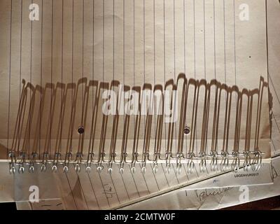 Long shadows from metal loops of ring bound notepad stretch across the lines of the ruled page in early evening low sunshine creating a strong pattern Stock Photo