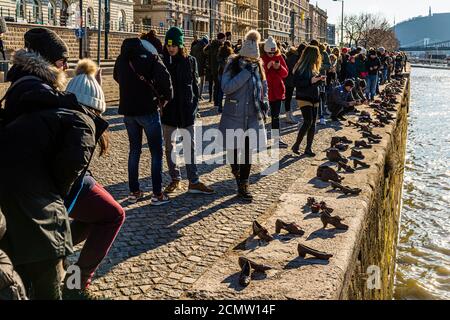Dozens of iron shoes commemorate the victims of the Arrow Cross militia on the Danube bank in Budapest, Hungary. In the winter of 1944-45, the fascist militiamen forced thousands of Jews and other persecuted people to take off their shoes on the riverbank before shooting them into the Danube — footwear was valuable and was looted. Film director Can Togay and sculptor Gyula Pauer created the memorial, unveiled in 2005; visitors examine the shoes cast into the stone embankment along the promenade. Stock Photo