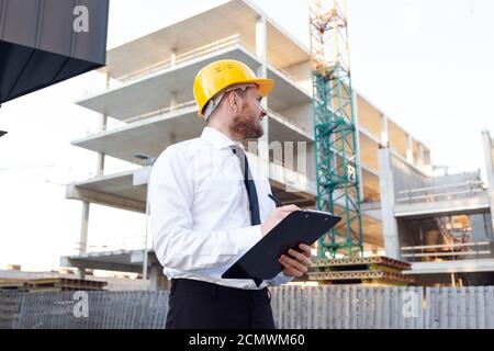Man Controlling Building. Builder making marks in Clipboard. House Building Stock Photo