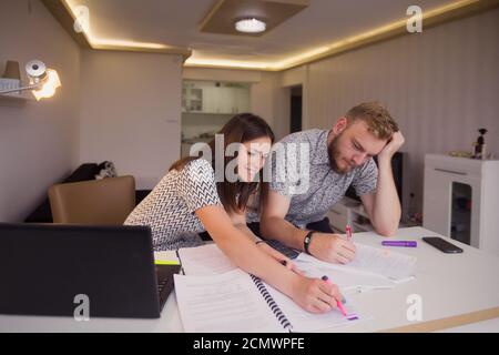 two young people, alone in room, styling together on a project, many papers on desk. Stock Photo