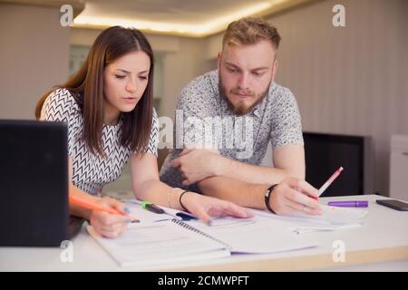 two young people, studying together, sitting in front of notes on a desk. Stock Photo