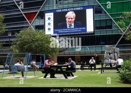 Workers take their lunch outdoors as a screen giving information about British Prime Minister Boris Johnson is seen on the background on the first day of 'circuit breaker' measures to curb coronavirus (COVID-19) at the central business district in Singapore, April 7, 2020. REUTERS/Edgar Su