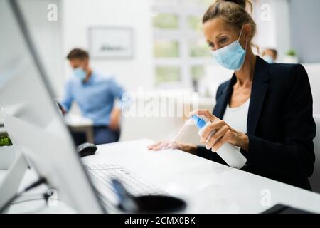 Woman Cleaning Desk In Office Using Alcohol Disinfectant Stock Photo
