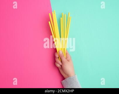 hand holds a stack of yellow paper tubes for a cocktail on a multi-colored background Stock Photo
