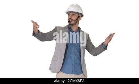 Architect man in helmet and head set talking to camera and making gestures showing on some objects on white background. Stock Photo