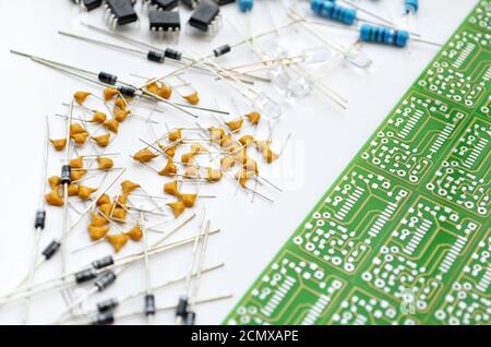 Set of various electronic components arranged near green electronic circuit board on white background. Close-up, selective focus Stock Photo