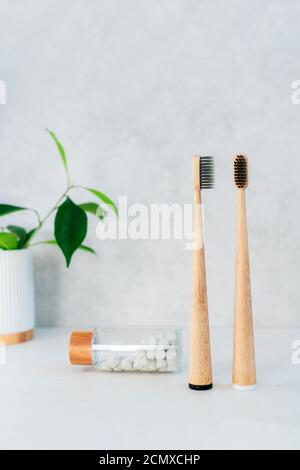 Zero waste bathroom items. Bamboo toothbrushes in recycling material holder, natural mouthwashing tabs and fresh green plants in glass. Oral care Stock Photo