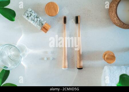 Top view zero waste bathroom items. Bamboo toothbrushes, natural mouthwashing tabs, fresh green leaves and glass of water on light background. Oral Stock Photo