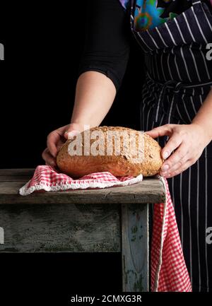 A baker woman holds fresh bread in her hand against the background of bakers  working in a bakery Stock Photo - Alamy