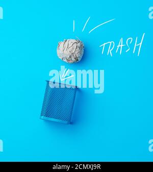 ball of crumpled gray paper and metal blue wastebasket Stock Photo