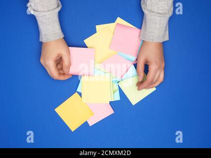 two female hands and many empty paper multi-colored stickers on a blue background Stock Photo