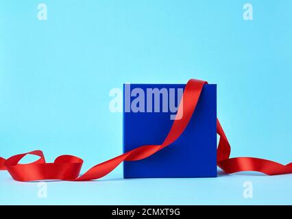 square blue cardboard box for a gift and twisted silk red ribbon on a blue background Stock Photo