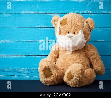 big teddy bear are sitting in white medical masks on a blue wooden background Stock Photo