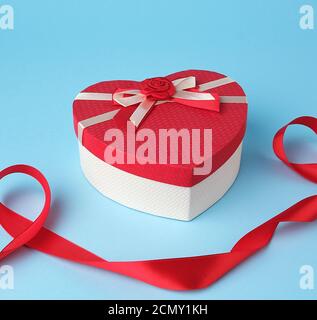 closed red heart-shaped gift box with a bow on a blue background Stock Photo