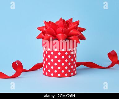 round red cardboard box in white polka dots on top of a bow on a blue background Stock Photo