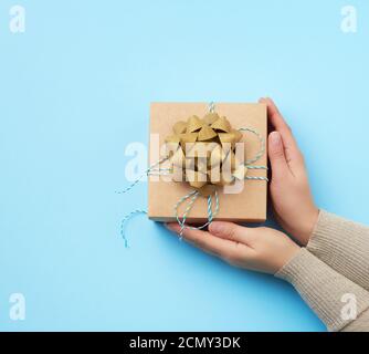 female hand holds a square box with a bow on a blue background Stock Photo