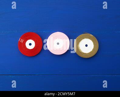 twisted red, pink, golden silk ribbons on a blue background Stock Photo