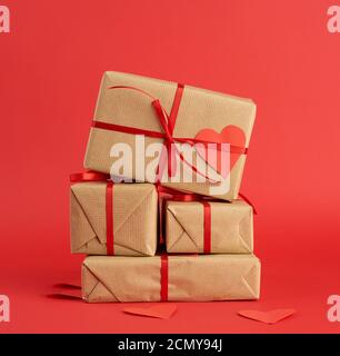 stack of wrapped gifts in brown craft paper and tied with a red ribbon on red Stock Photo