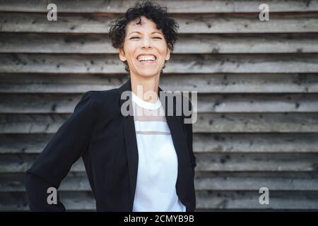 Portrait of cheerful female entrepreneur wearing suit while standing against wall Stock Photo