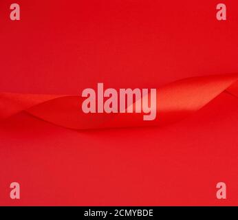 twisted red silk shiny ribbon on a red background, festive design element Stock Photo