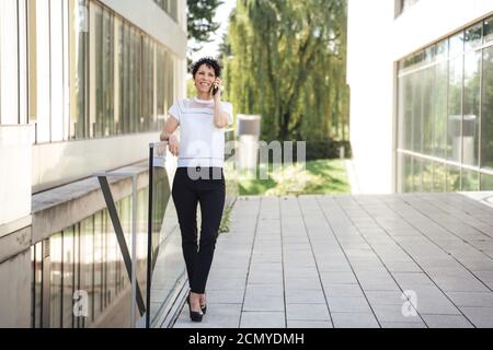 Full length of businesswoman standing by railing while talking on mobile phone outside near office Stock Photo