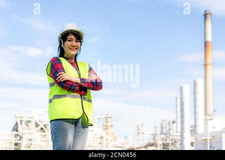 Asian woman engineer arm crossed and smile with confident looking forward to future with oil refinery plant factory in background. Stock Photo