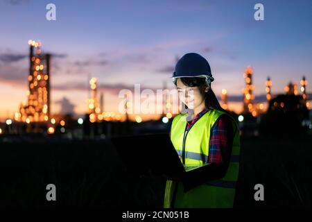 Asian woman petrochemical engineer working at night with notebook Inside oil and gas refinery plant industry factory at night for inspector safety qua Stock Photo