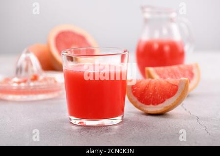A glass of freshly made grapefruit juice and slices of fresh fruit on a light concrete background. H Stock Photo