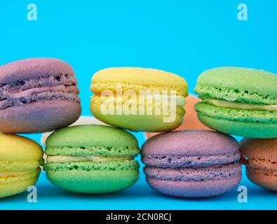 multi-colored round baked macarons cakes on a light blue background, dessert stands in a row Stock Photo