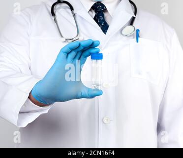 doctor in a white coat and blue sterile latex gloves holds a plastic jar for stool analysis Stock Photo