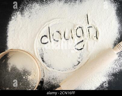 sprinkled white wheat flour on a black table and the inscription dough Stock Photo