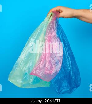 hand holds empty multi-colored plastic bags on a blue background Stock Photo