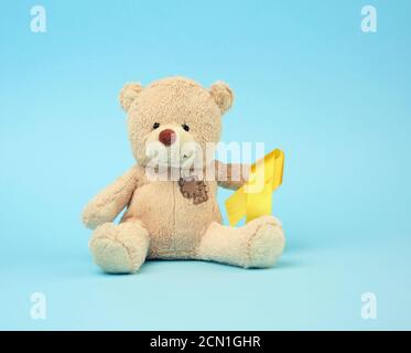 Cute brown teddy bear with a patch holds a silk yellow ribbon in the shape of a loop Stock Photo