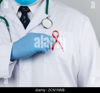 doctor in a white coat and tie is standing on a white background, red silk ribbon is hanging on his Stock Photo