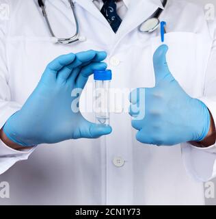 doctor in a white coat and blue sterile latex gloves holds a plastic jar for stool analysis Stock Photo