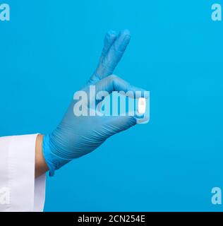 hand in blue sterile gloves holds an oval white pill Stock Photo