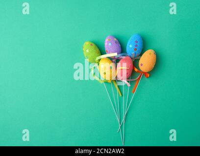 multi-colored decorative Easter eggs on sticks on a green background, festive backdrop, top view Stock Photo