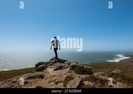 Lone person walking on rocks on headlands over looking Pacific Ocean Stock Photo