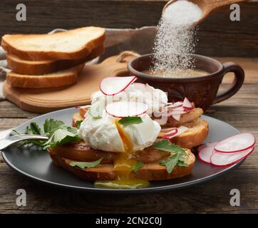 two sandwiches on a toasted white slice of bread with poached eggs, green leaves of arugula and radi Stock Photo