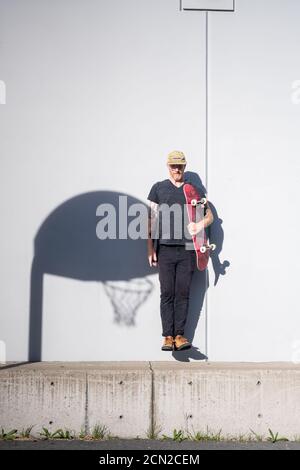 Portrait of adult male jumping holding skateboard in bright sunlight Stock Photo