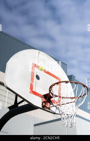 Tennis ball hitting backboard on basketball hoop under cloudy sky Stock Photo