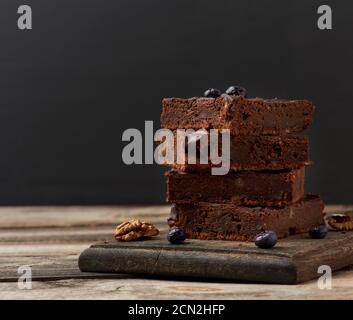 stack of square baked slices of brownie chocolate cake with walnuts on a wooden surface. Cooked home Stock Photo
