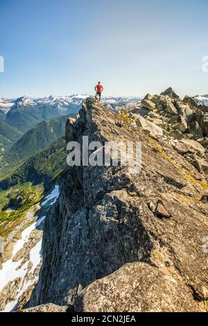 Trail runner stands on mountain summit, edge of a cliff. Stock Photo
