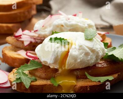 sandwich on toasted white slice of bread with poached eggs, green leaves of arugula and radish Stock Photo