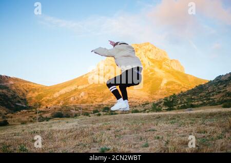 back view of unrecognizable male in casual clothes jumping high against mountains Stock Photo