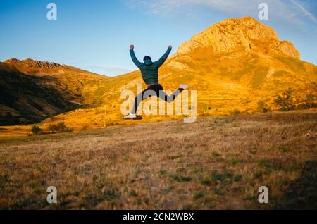 back view of unrecognizable male in casual clothes jumping high against mountains Stock Photo