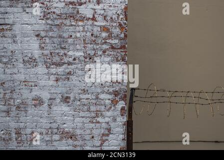 Half a brick wall with barbed wire next to it Stock Photo