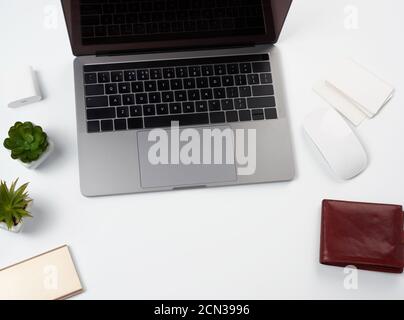 open gray laptop stands on a white table, next to a wireless mouse, freelancer workplace, businessma Stock Photo