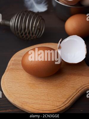 brown whole chicken eggs on a wooden board, behind a whisk for whipping Stock Photo