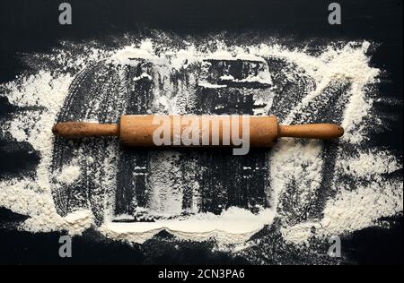 white wheat flour scattered on a black table and a wooden rolling pin on a black table Stock Photo
